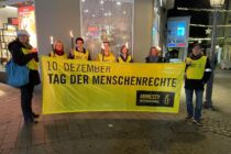 Sieben Mitglieder der Ratinger Gruppe mit Fackeln und hinter dem Banner "10. Dezember - Tag der Menschenrechte"