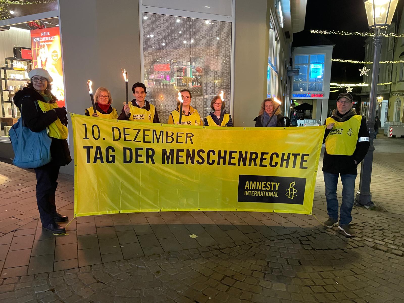 Sieben Mitglieder der Ratinger Gruppe mit Fackeln und hinter dem Banner "10. Dezember - Tag der Menschenrechte"